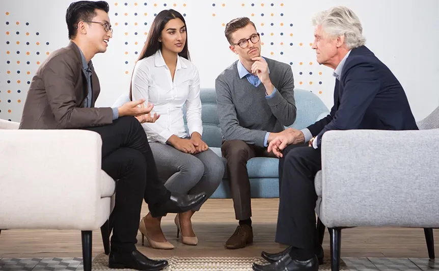 Four people in business attire sit in a small discussion circle in an office lounge