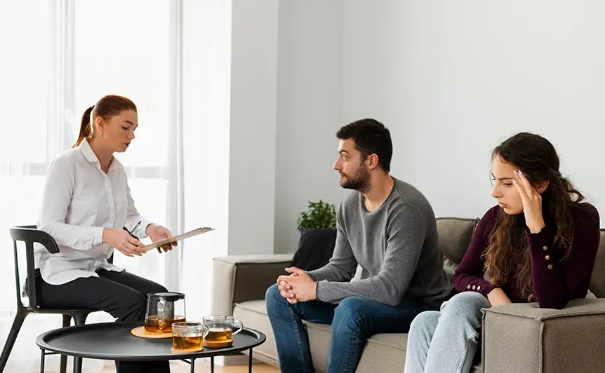 Woman speaking with two seated people in a modern living room during a counseling session