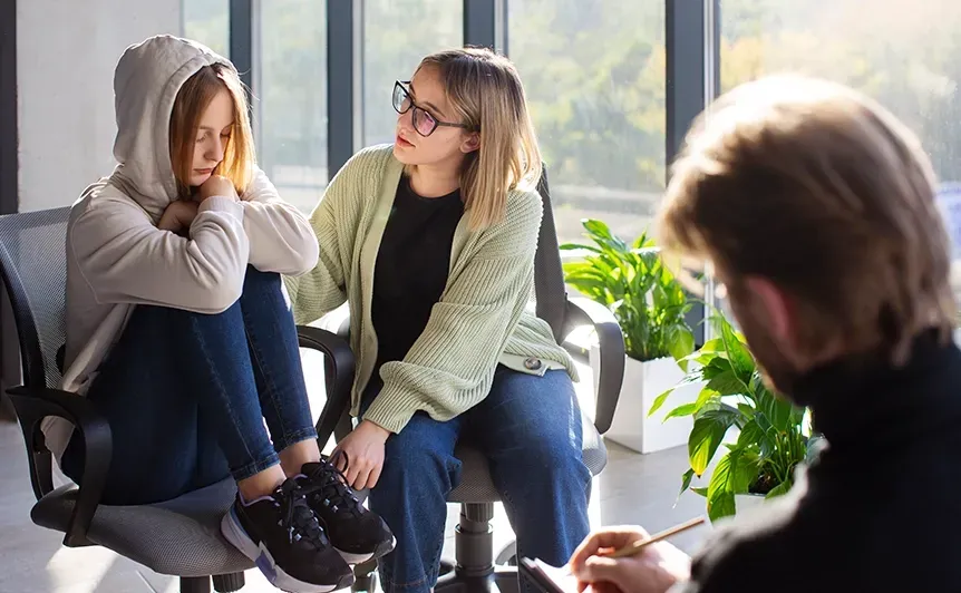 Two people sit on a couch talking with a counselor in a bright living room