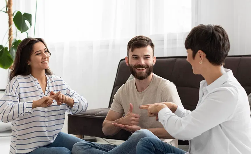Three people chatting and smiling in a bright living room on a couch.