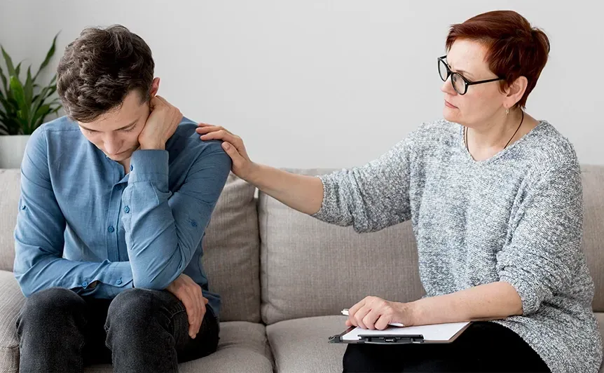 Counselor comforts a distressed client on a couch during a discussion.