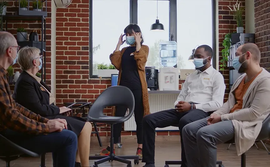 Small group meeting in a modern office, with a presenter and seated people wearing face masks.