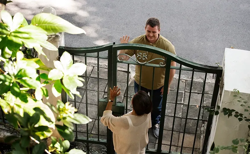 Two people opening a dark green metal gate from opposite sides, viewed from above.