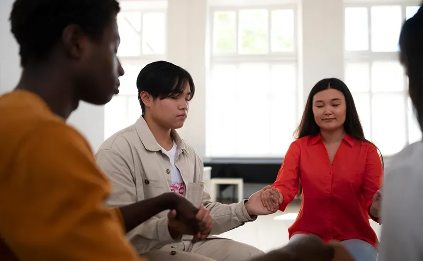 Three people seated in a bright room, one holding a paper and a woman in a red blouse smiling.