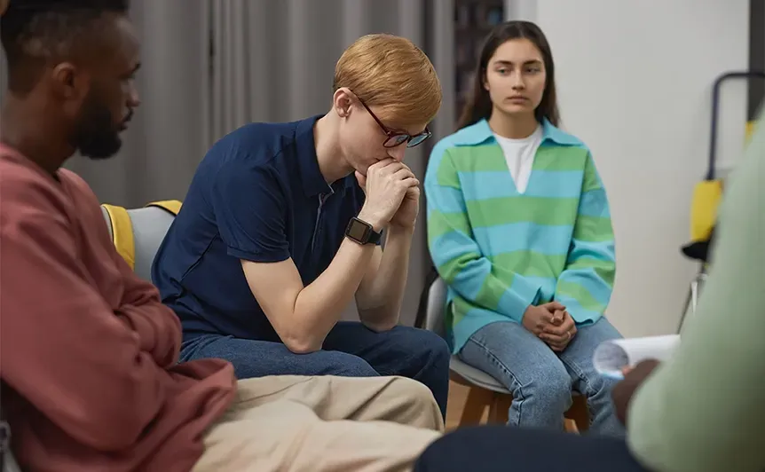 Three people seated in a counseling group, one man resting his hand on his chin.