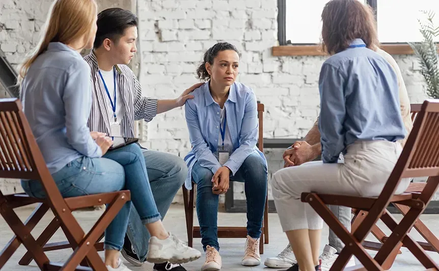 Four people in blue shirts sit in a circle discussing in a bright office room