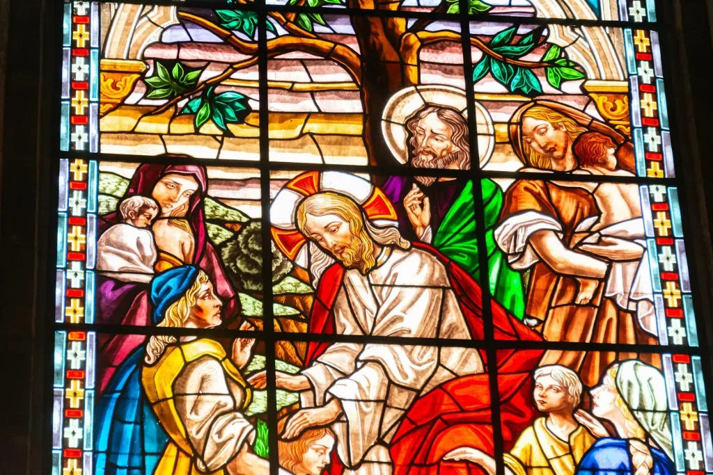 Stained-glass biblical scene with robed figures gathered around a seated central figure, in bright reds and blues