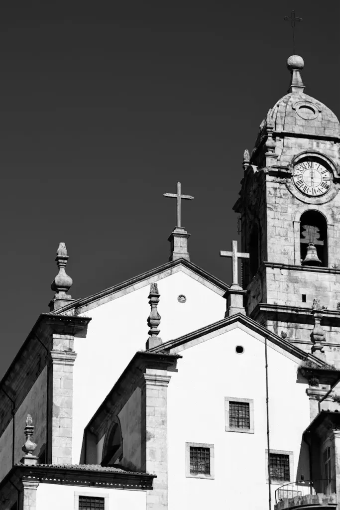 Black-and-white view of a church with a cross-topped roof and tall bell tower against the sky