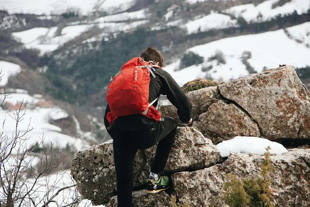 Hiker with red backpack climbing snowy rocks in a mountain landscape