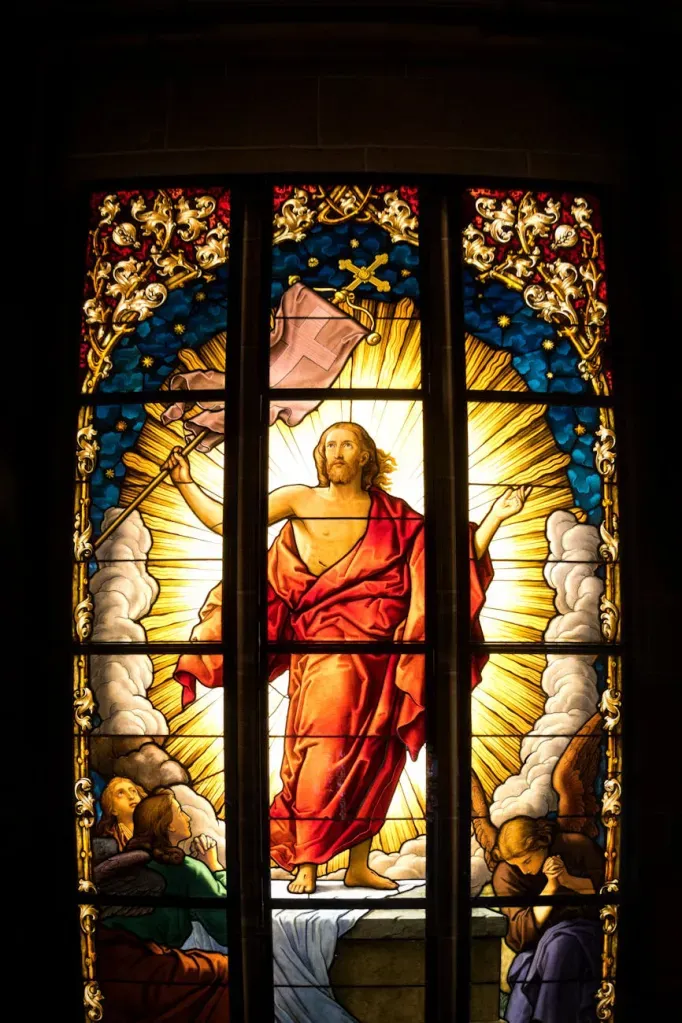 Stained glass window depicting Jesus in a red robe with a golden halo, surrounded by clouds and light