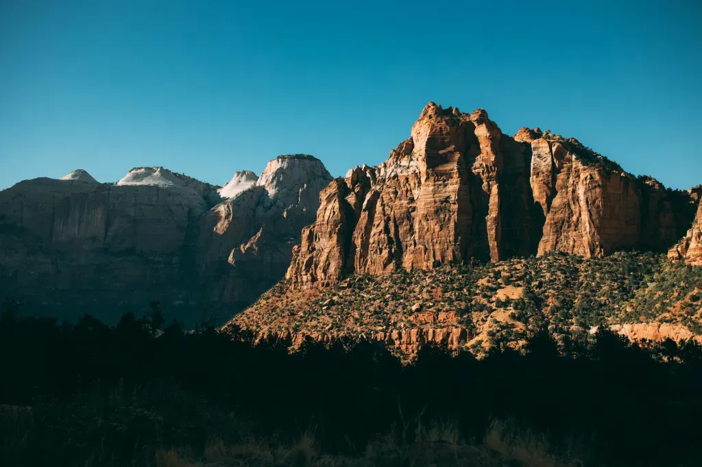 Sunlit rocky mountain cliffs above a dark forest at dusk