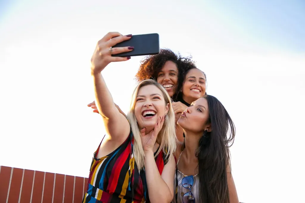 Four friends taking a selfie outdoors, smiling and posing in bright sunlight