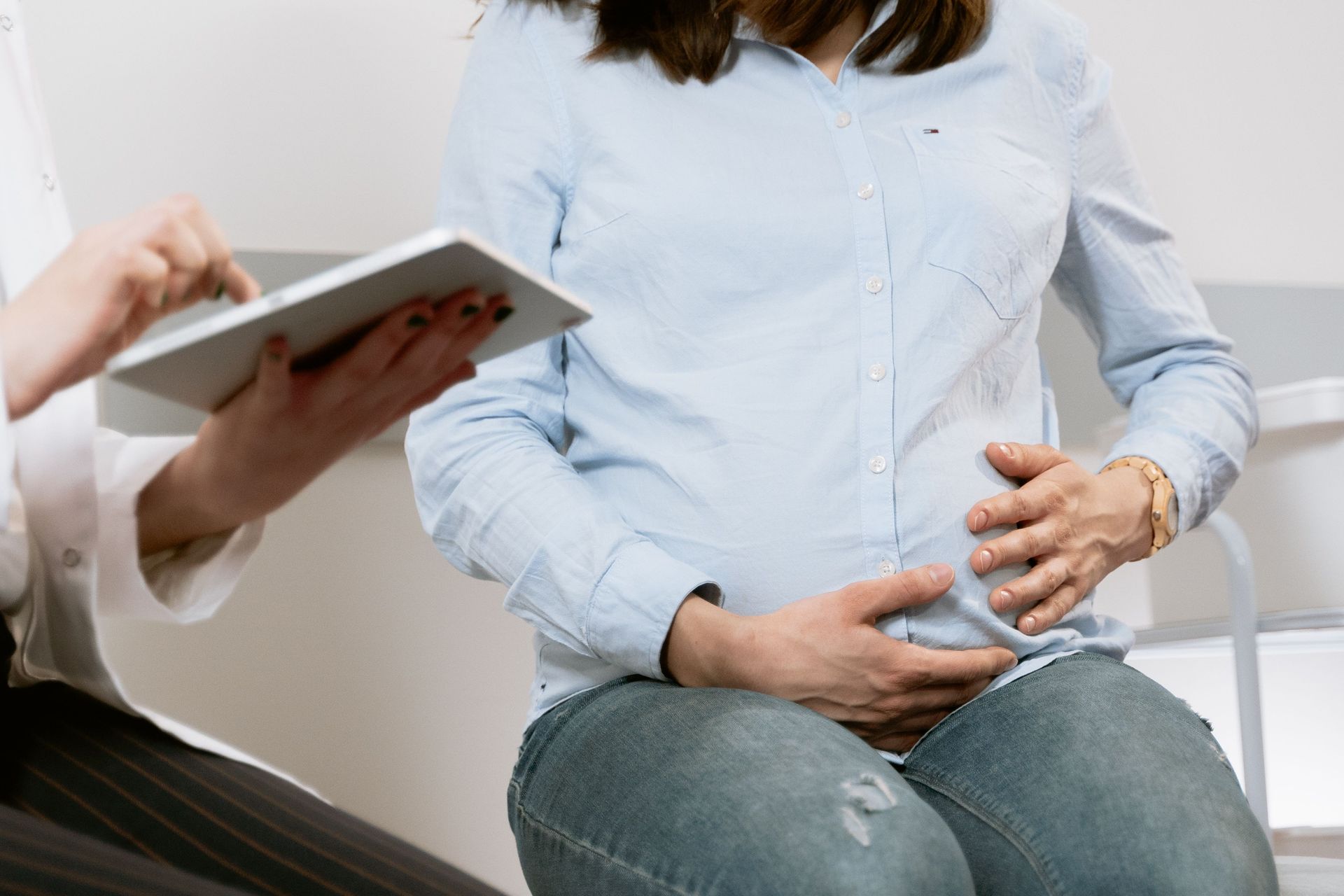 Doctor examining a pregnant patient holding her belly while seated indoors