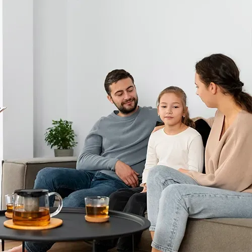 Three people sitting on a couch beside a coffee table with tea in a bright living room