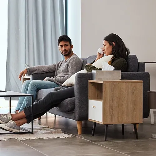 Two people relaxing on a gray sofa in a bright living room, with a small wooden side table nearby