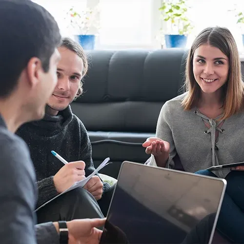 Three people in a meeting around a laptop, discussing notes in a bright office