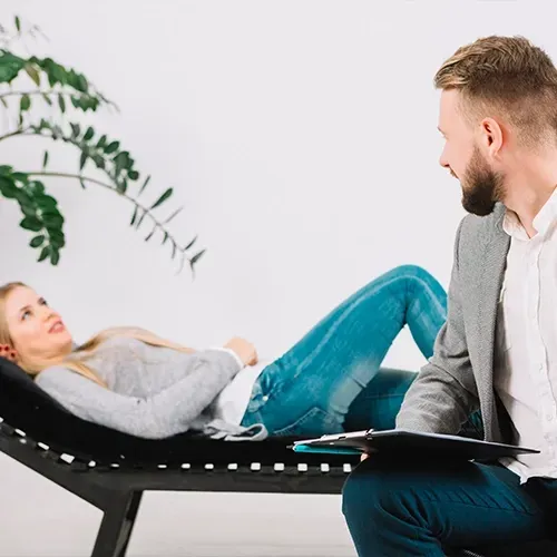 Woman reclining on a black lounge chair, talking with a seated man in a bright office.