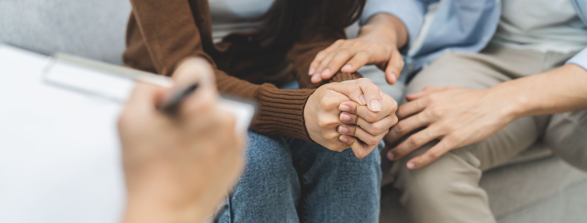 People seated in a counseling session, with one holding a pen and another clasping hands.