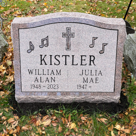 A double-slab granite headstone in a cemetery with a cross and musical notes.