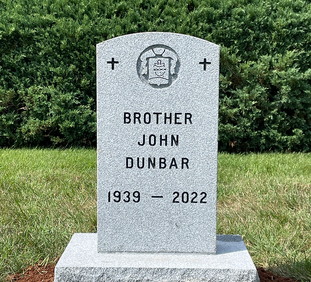 Gray granite tombstone. Includes cross symbols and emblem, set in grass.