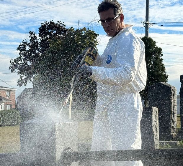 Worker power washing a fence post at a cemetery