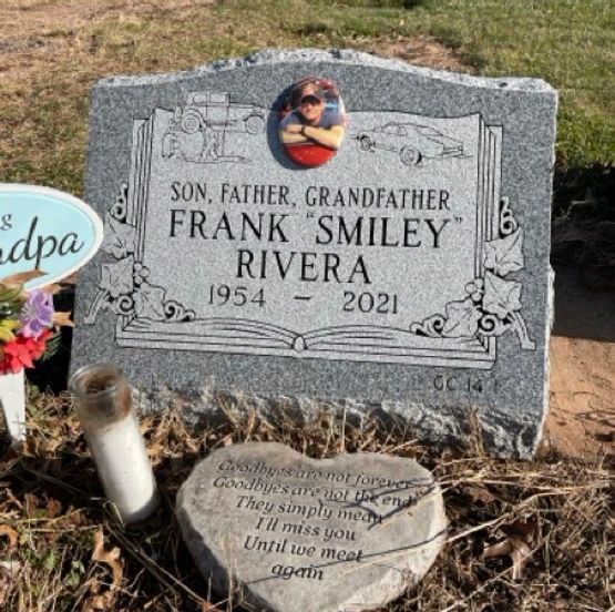 A single upright grey headstone with a memorial portrait centered over a decorative book. 