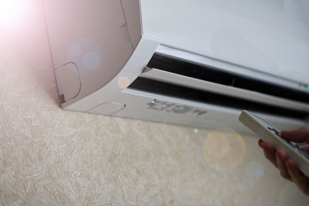 A Person Is Using A Remote Control To Turn On An Air Conditioner — Newcastle Air & Refrigeration In Newcastle, NSW