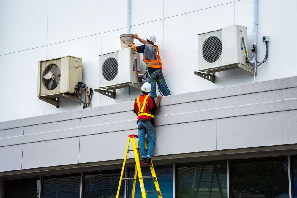 Two Men Are Working On Air Conditioners On The Side Of A Building — Newcastle Air & Refrigeration In Merewether, NSW