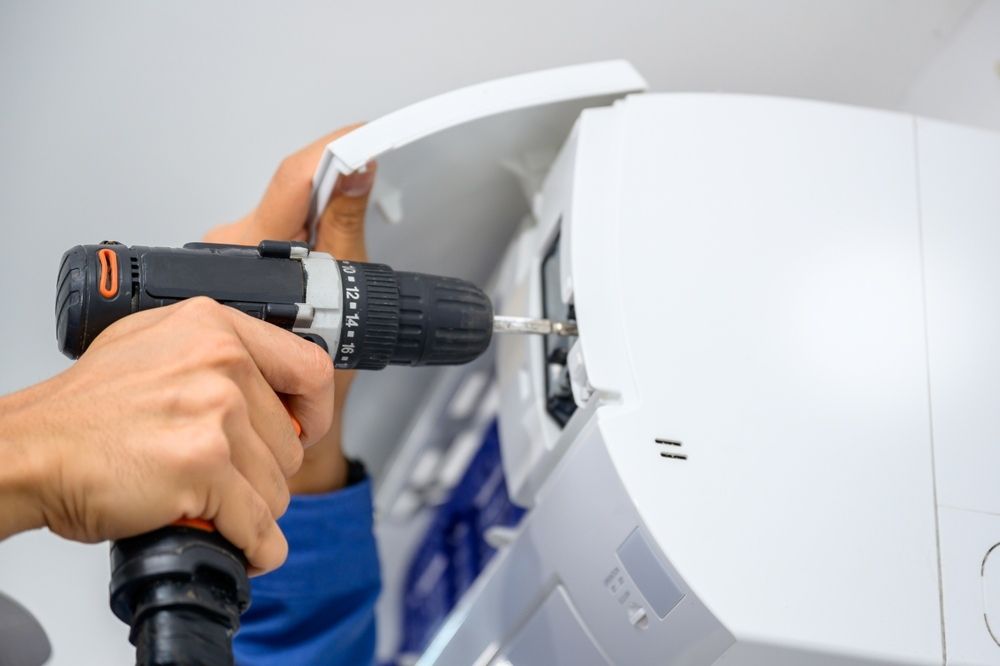 A Person Is Using A Drill To Fix An Air Conditioner — Newcastle Air & Refrigeration In Newcastle, NSW