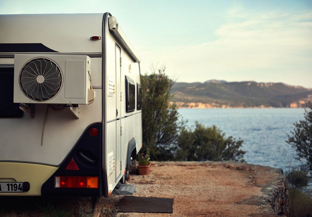 A Rv With A Fan On The Side Is Parked Next To A Body Of Water — Newcastle Air & Refrigeration In Newcastle, NSW