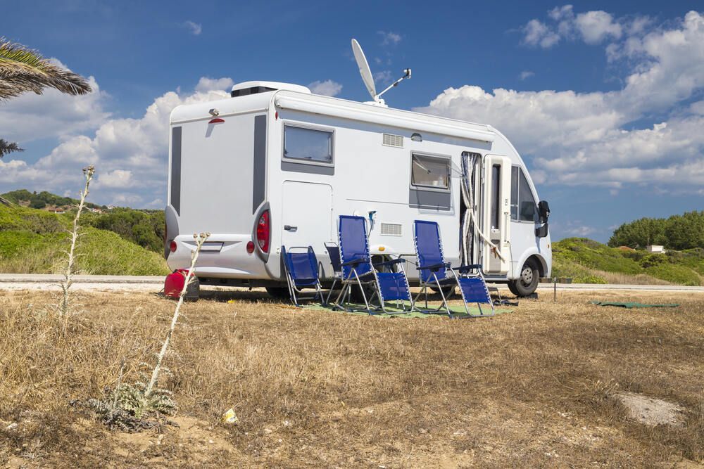 A RV Is Parked In A Field With Chairs And A Table — Newcastle Air & Refrigeration In Newcastle, NSW