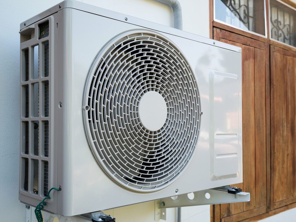 A White Air Conditioner Is Mounted On The Side Of A Building — Newcastle Air & Refrigeration In Newcastle, NSW