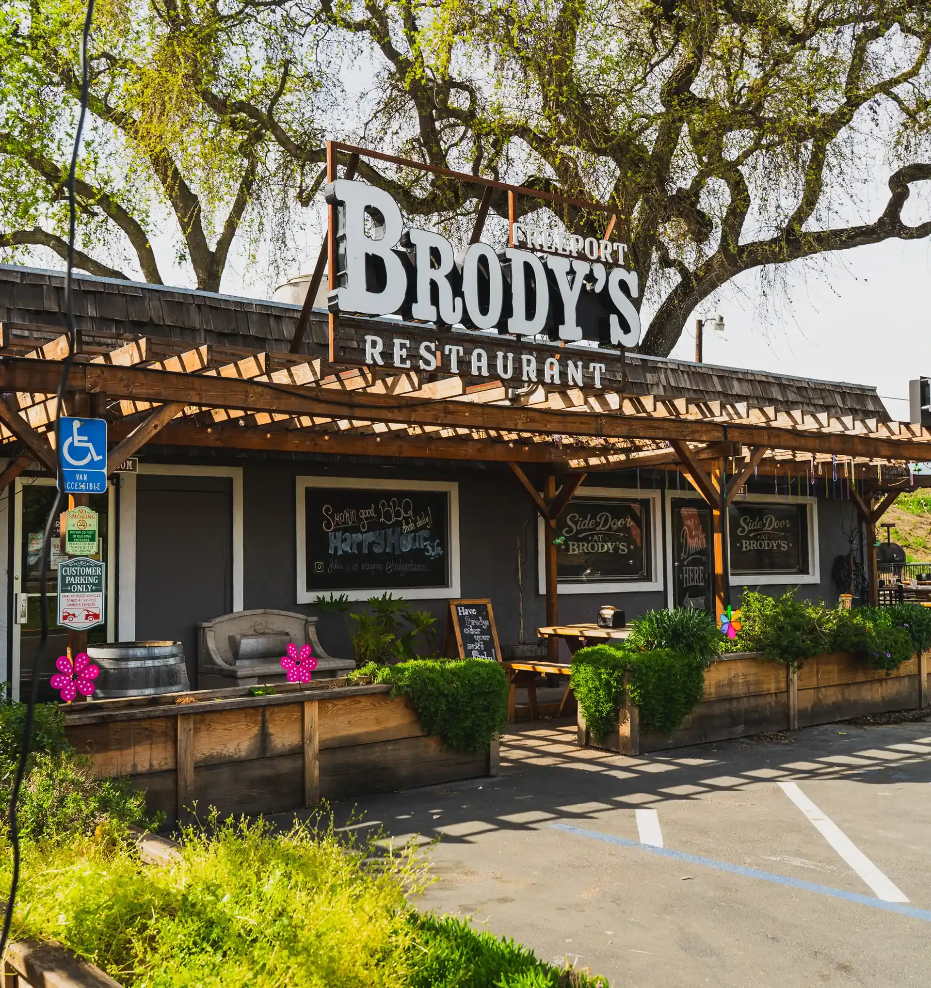 Brody’s Restaurant storefront with patio seating, trees overhead, and a wheelchair-accessible parking sign