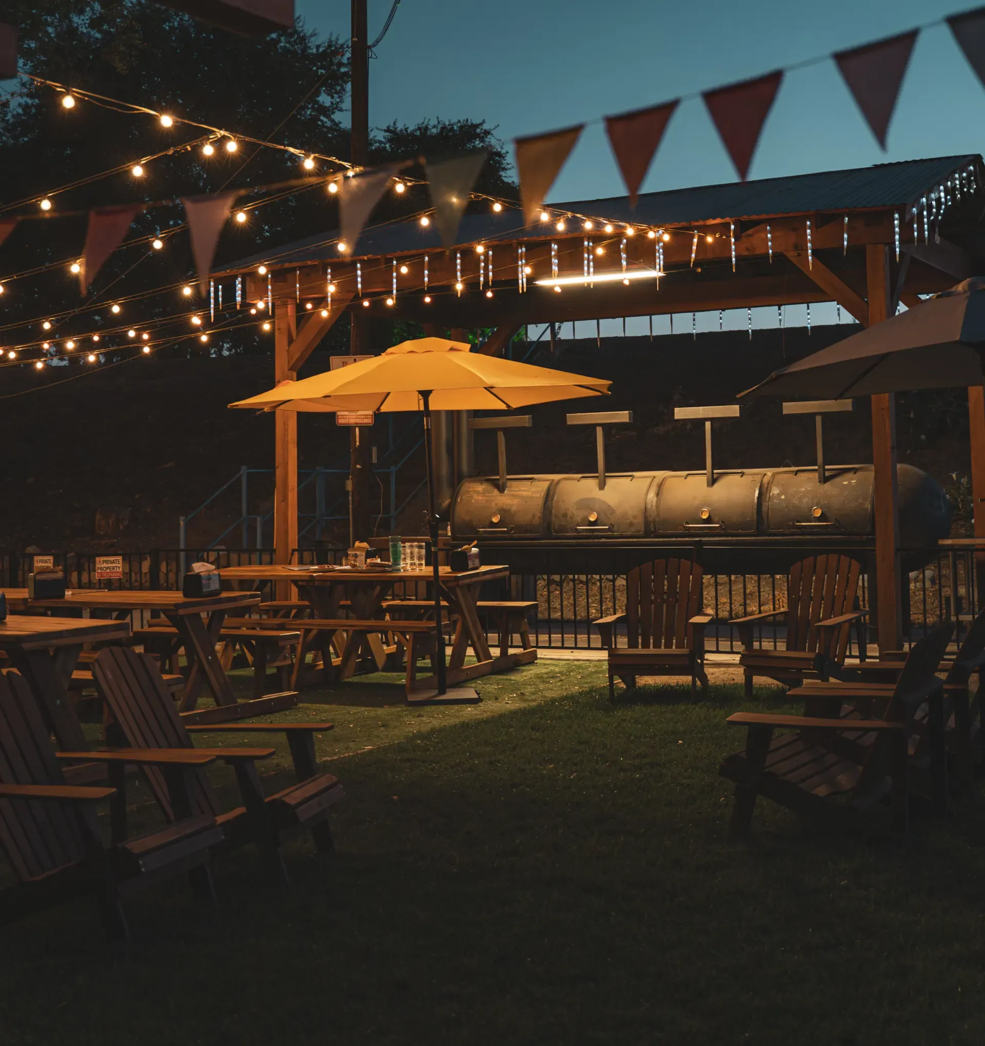 Outdoor patio with string lights, yellow umbrellas, and wooden tables and chairs at dusk