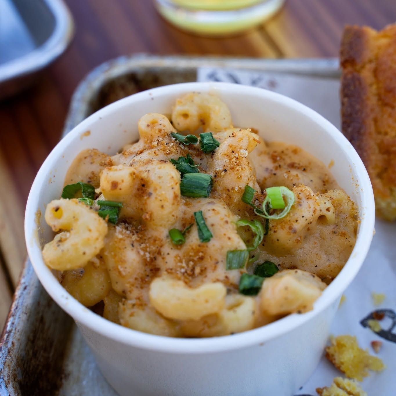 Mac and cheese in a white cup, topped with herbs and pepper on a table