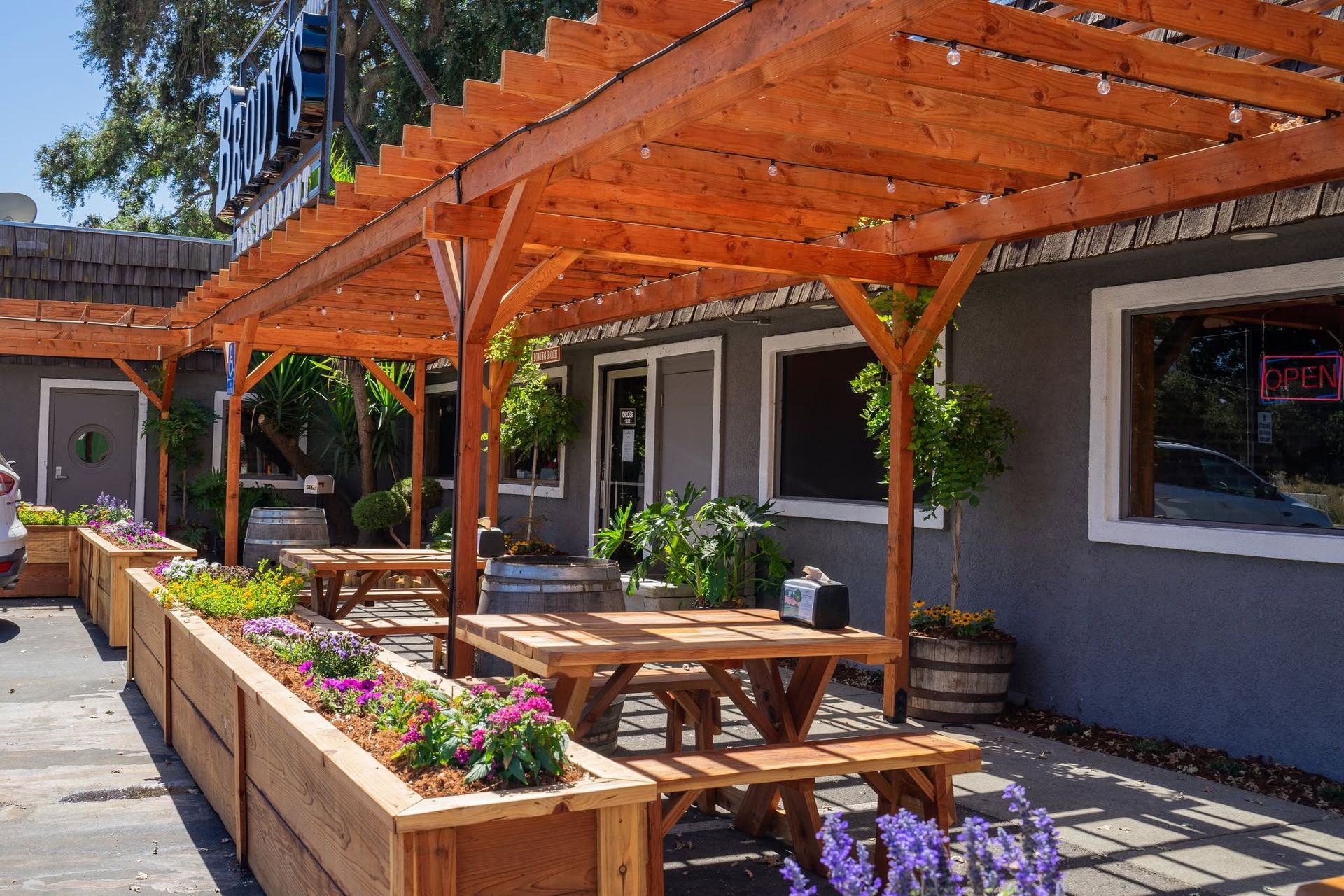 Patio with wooden pergola, picnic tables, flower planters, and a modern building exterior