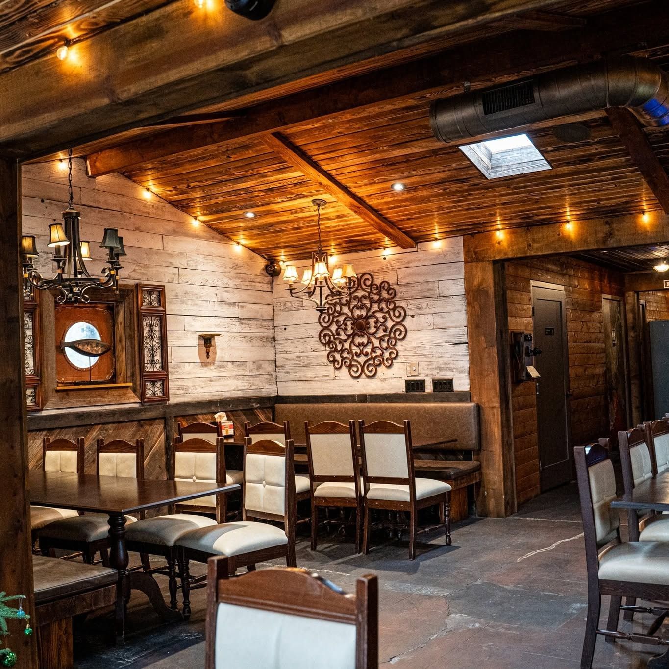 Rustic restaurant interior with wooden beams, warm lighting, brick walls, and empty tables and chairs
