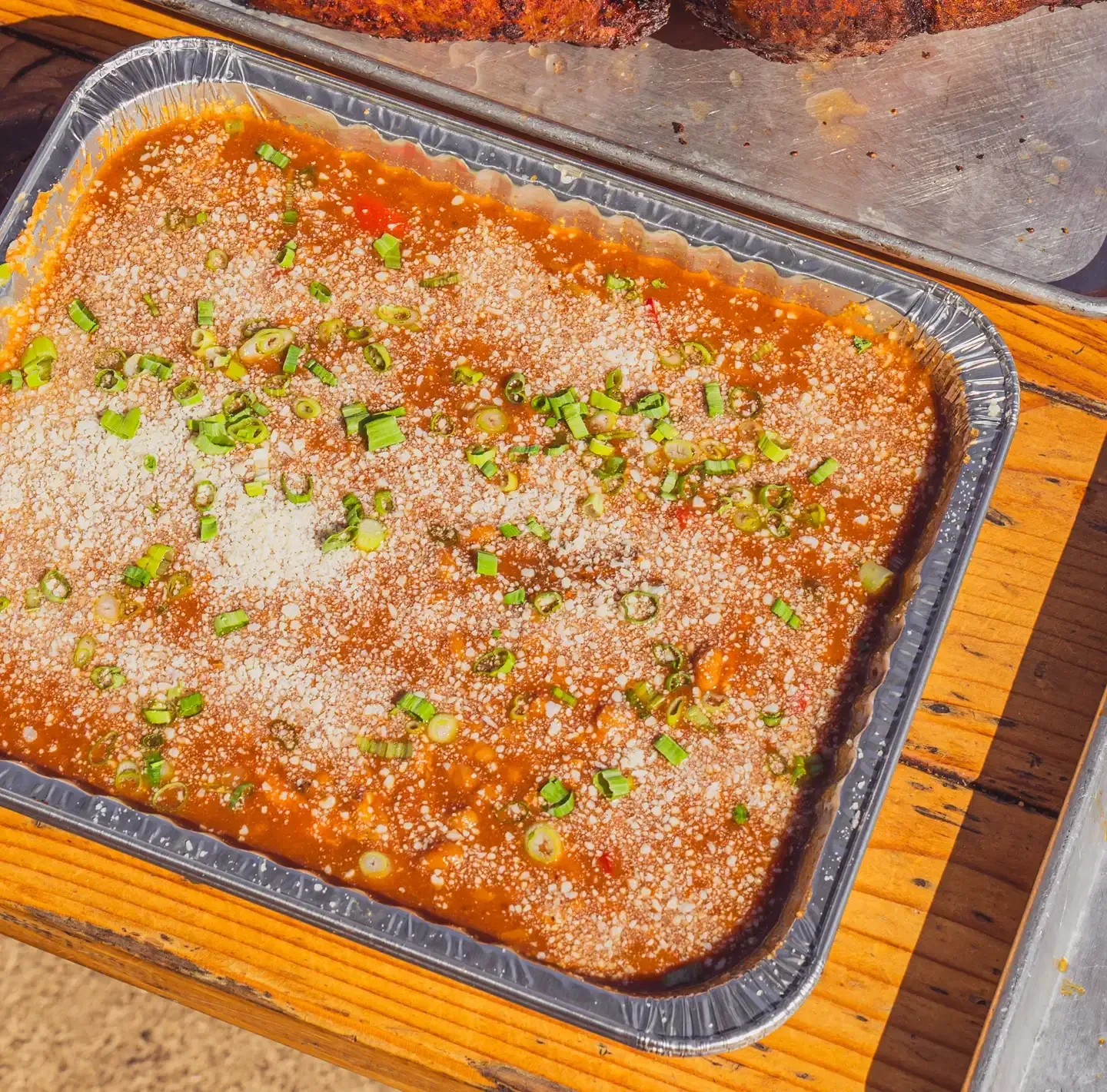 Tray of baked pasta with tomato sauce, melted cheese, and green garnish on a wooden table.