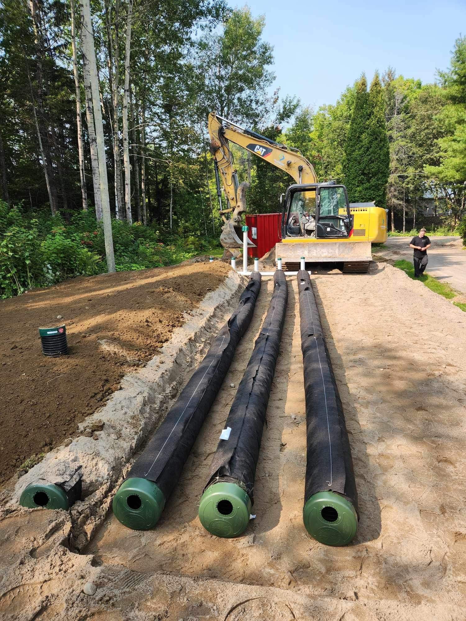 Une excavatrice jaune creuse un trou dans le sol à côté d'une rangée de tuyaux.