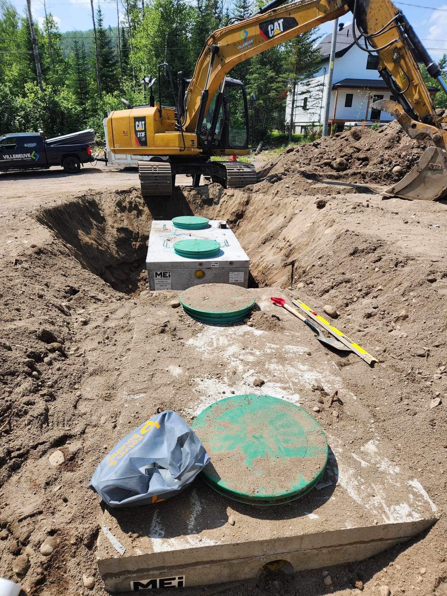 Une excavatrice jaune creuse un trou dans la terre à côté d'une fosse septique.