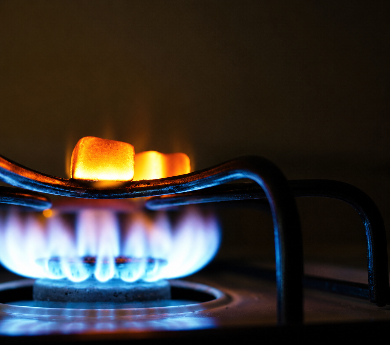 Blue gas stove flame heating two marshmallows on a fork over a burner