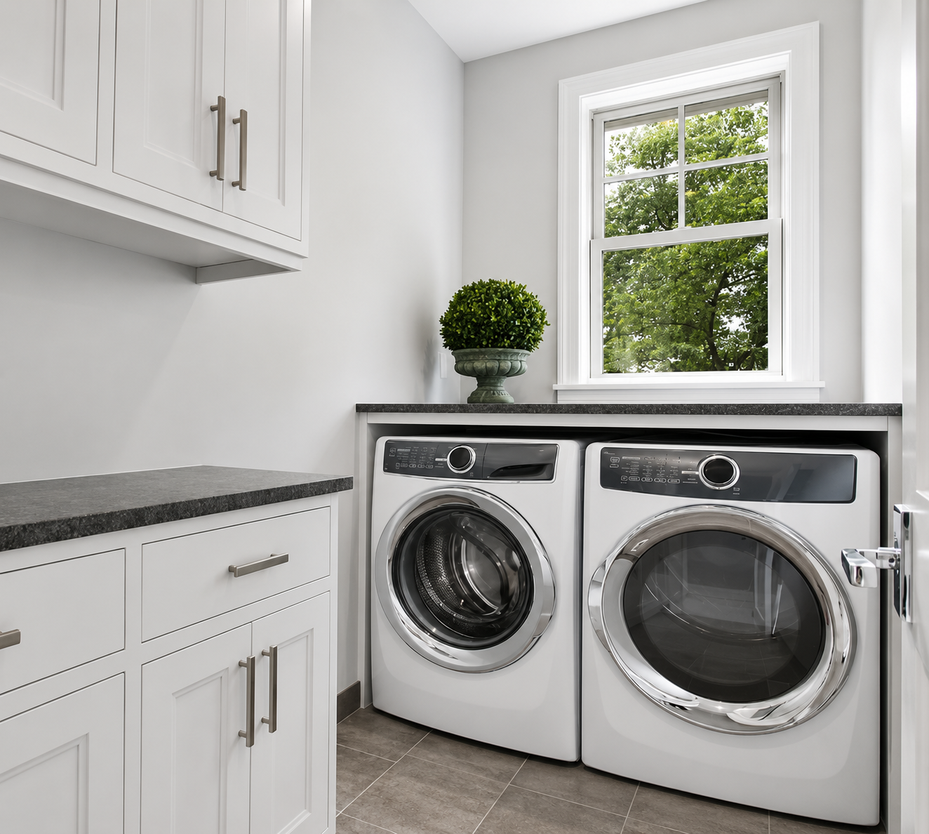 Bright laundry room with white washer and dryer, gray cabinets, and a window above the machines