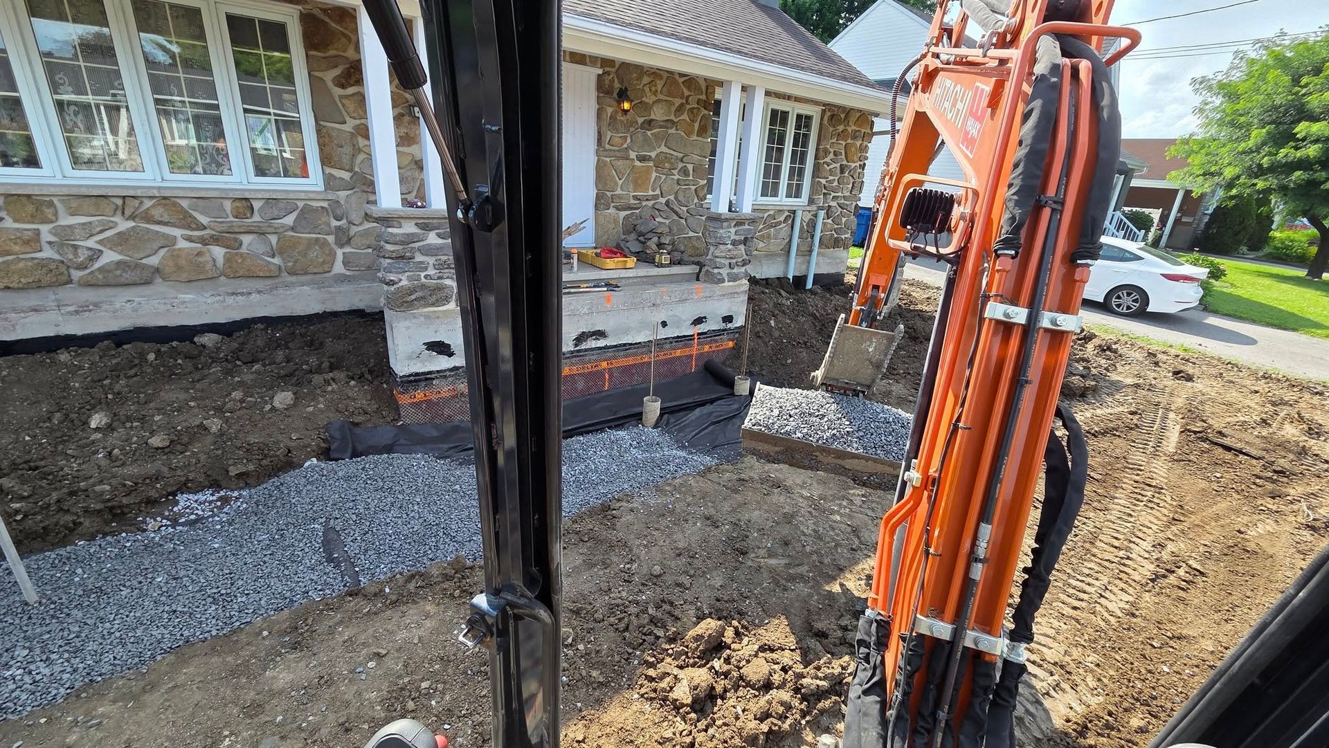 Une excavatrice creuse près d'une maison ; de la terre, du gravier et des matériaux de construction sont visibles.