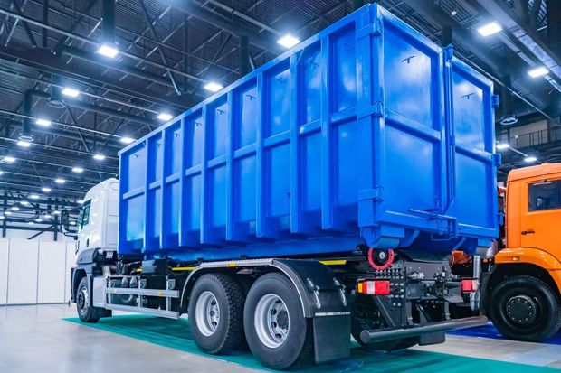 Benne à déchets industrielle bleue sur un semi-remorque dans un grand entrepôt.