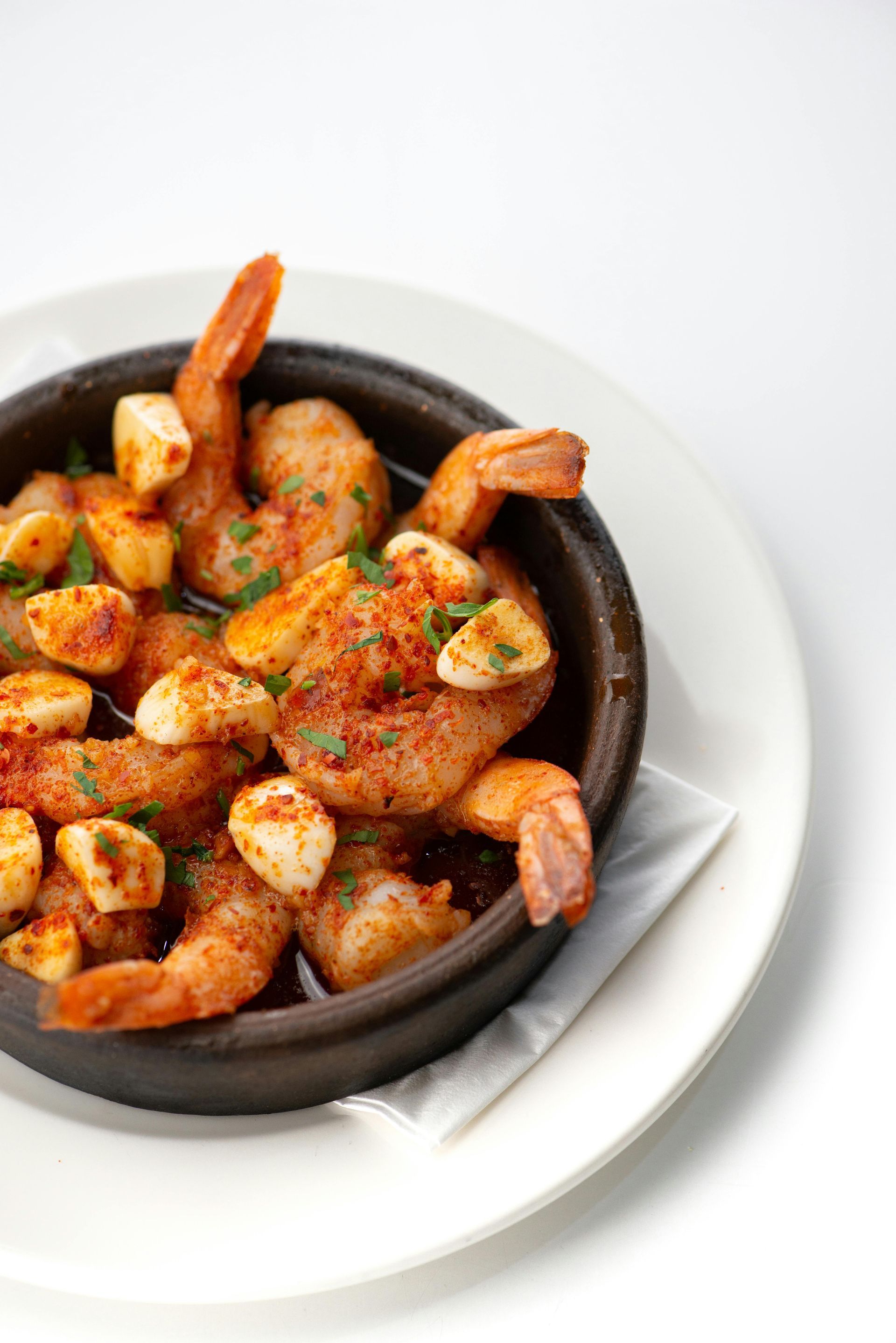 Gambas y pan de ajo en un bol negro sobre un plato blanco, adornado con hierbas y pimentón.