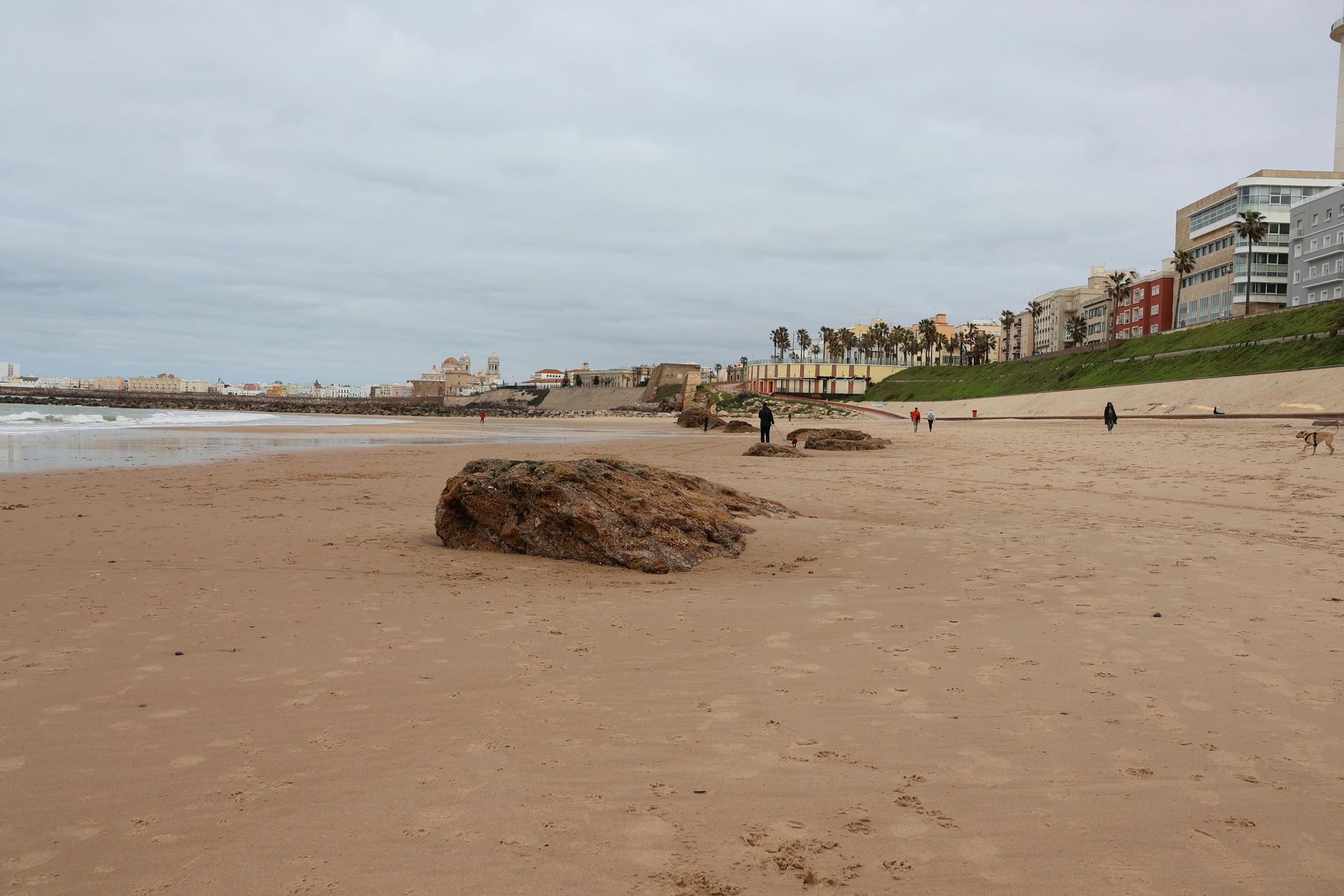 Acantilados rocosos junto al mar con vistas a una playa de arena y olas bajo un cielo nublado al atardecer.
