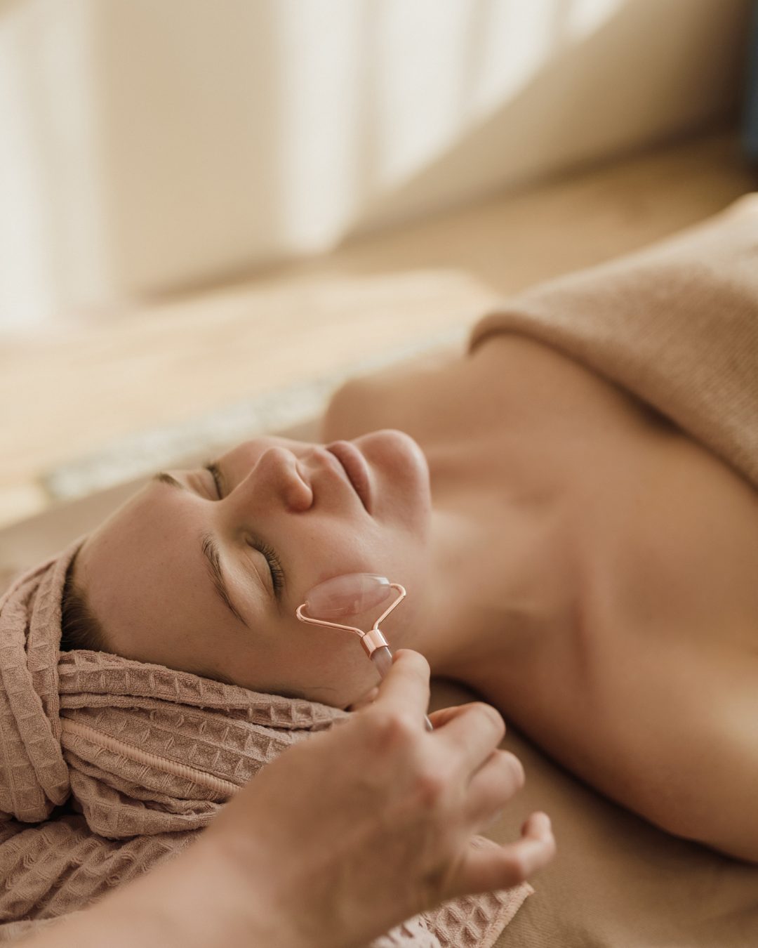 A person receives a facial massage with a pink quartz roller while lying down at a spa.