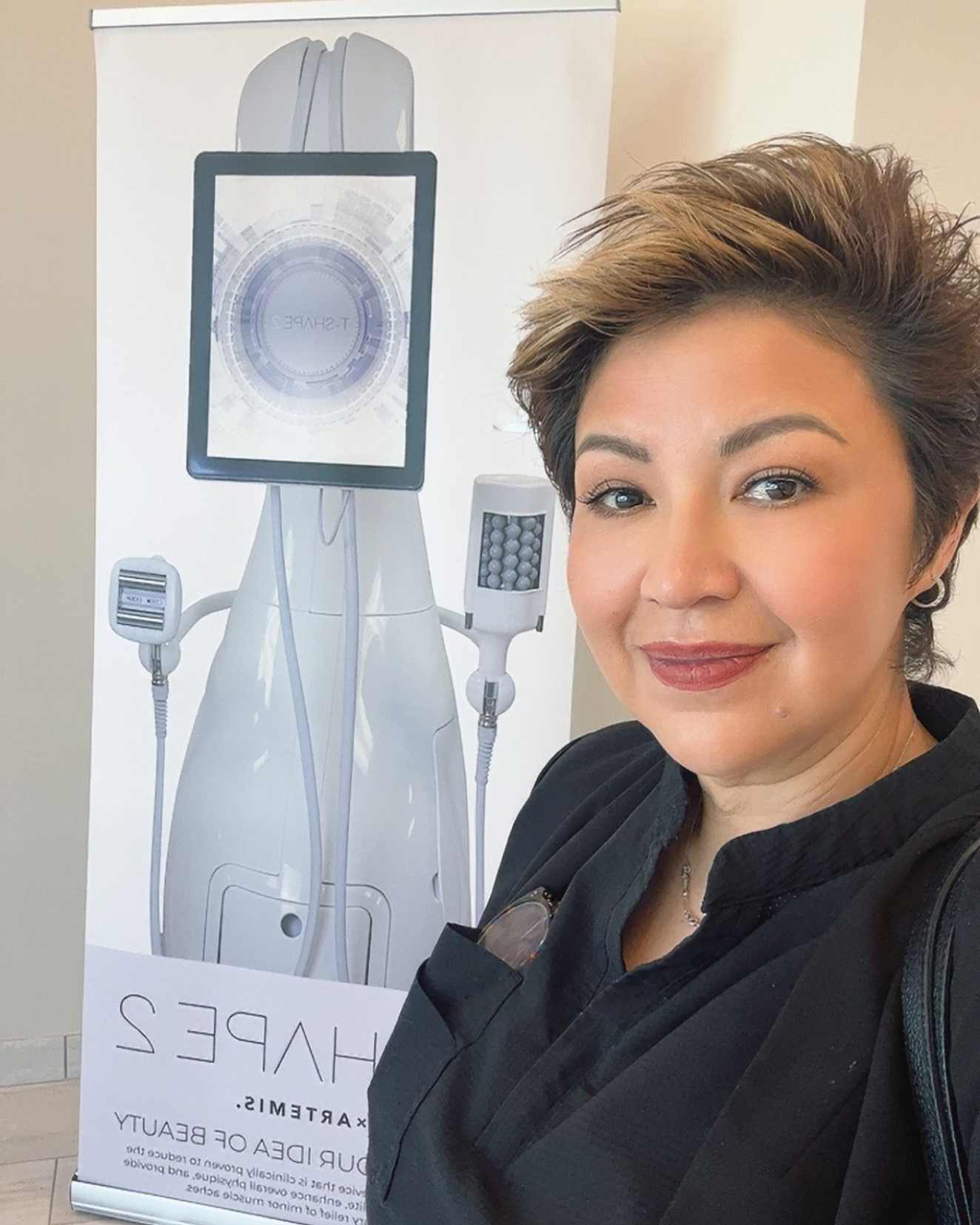 A person with short, light-brown hair smiles next to a promotional banner for a SHAPE 2 cosmetic machine.