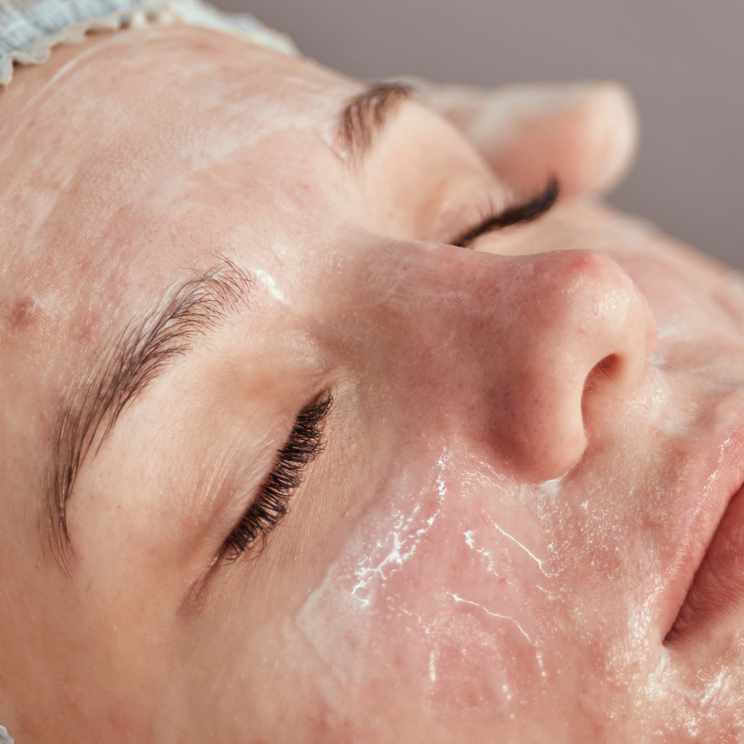 Close-up of a person lying down with closed eyes, receiving a professional skincare treatment with a clear gel mask applied.