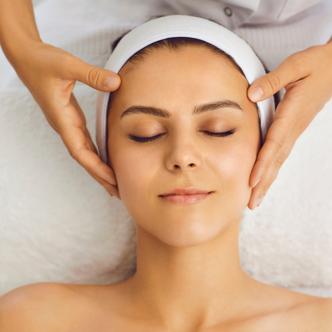 A person with eyes closed receives a gentle facial massage from a practitioner in a spa setting.